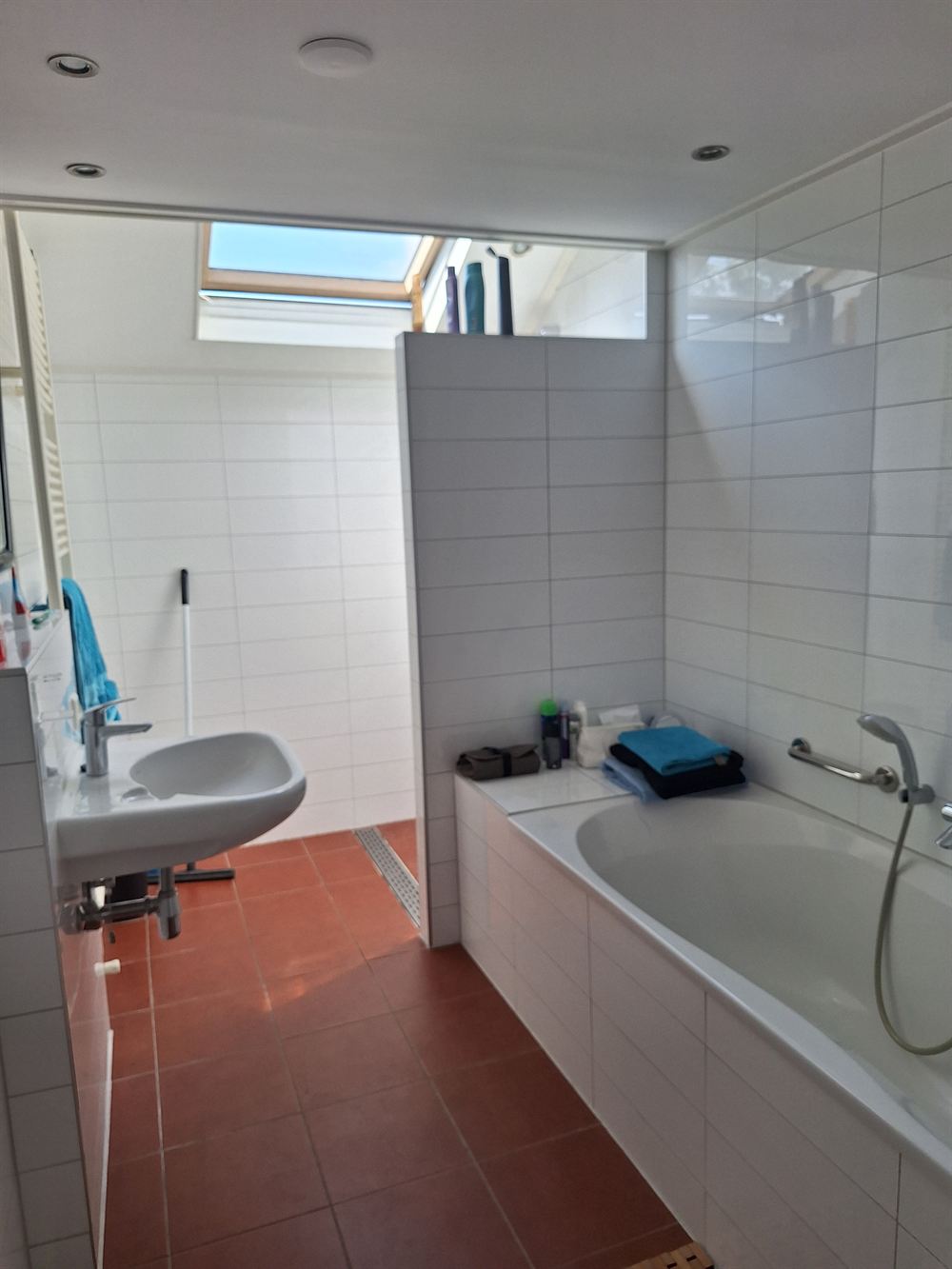 De badkamer met ligbad, wastafel en een terracotta tegelvloer