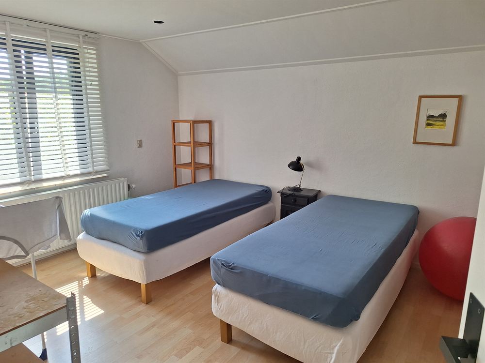 Slaapkamer met twee eenpersoonsbedden naast elkaar, een leeslamp en een ingelijste prent aan de wand