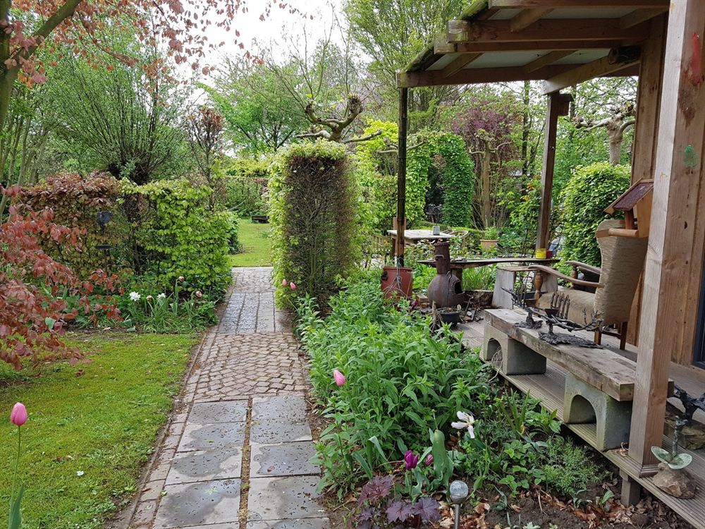 Klinkerpad door de tuin langs volle borders naar een houten overkapping met beelden