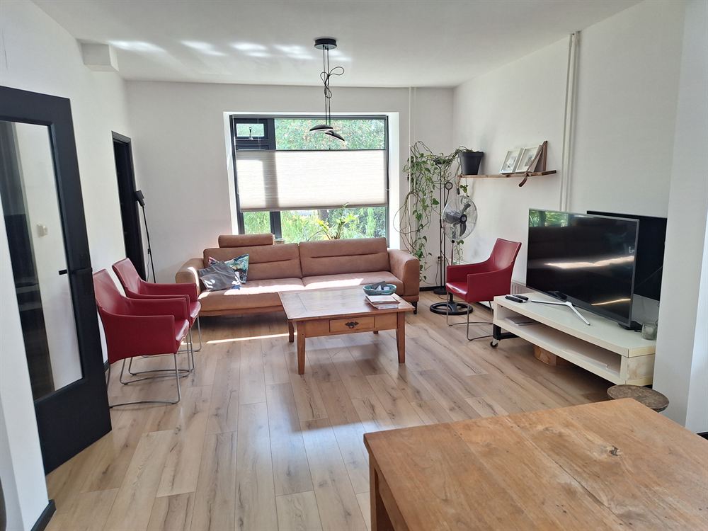 De woonkamer met bank, twee rode fauteuils en uitzicht op de tuin